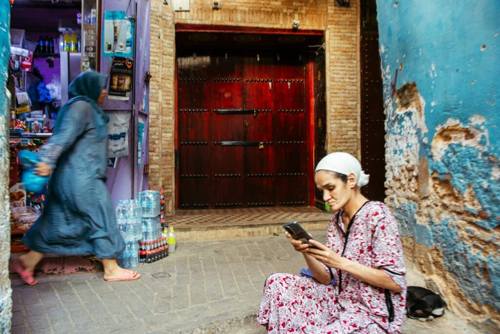 Woman sits while another walks in the alley.